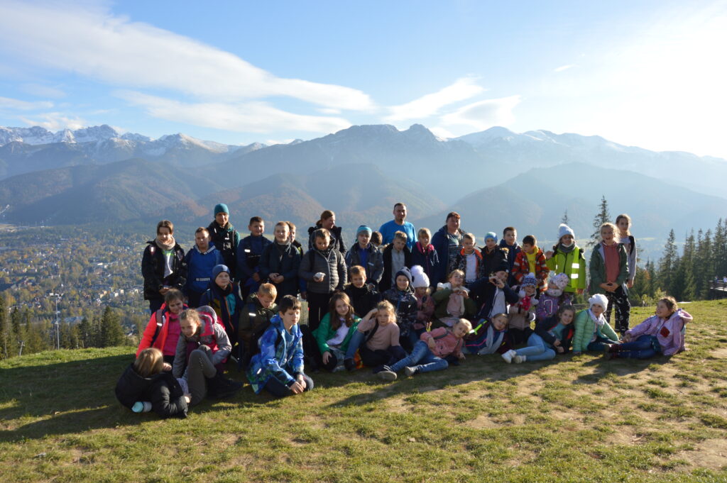 Grupa dzieci ze Szkoły Podstawowej w Kornatce wraz z nauczycielami na wycieczce, w tle góry